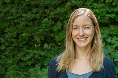 Erzieherin Sarah lächelt warmherzig in die Kamera; im Hintergrund eine grüne Hecke